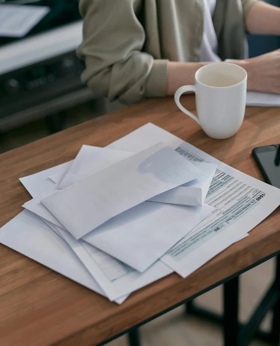 a woman sitting at a table with papers and a cup of coffee, delivering mail, multiple levels, white paper, press shot