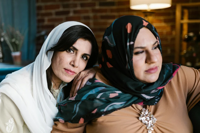 a couple of women sitting next to each other, a portrait, hurufiyya, arm around her neck, riyahd cassiem, half - body shot, fully covered