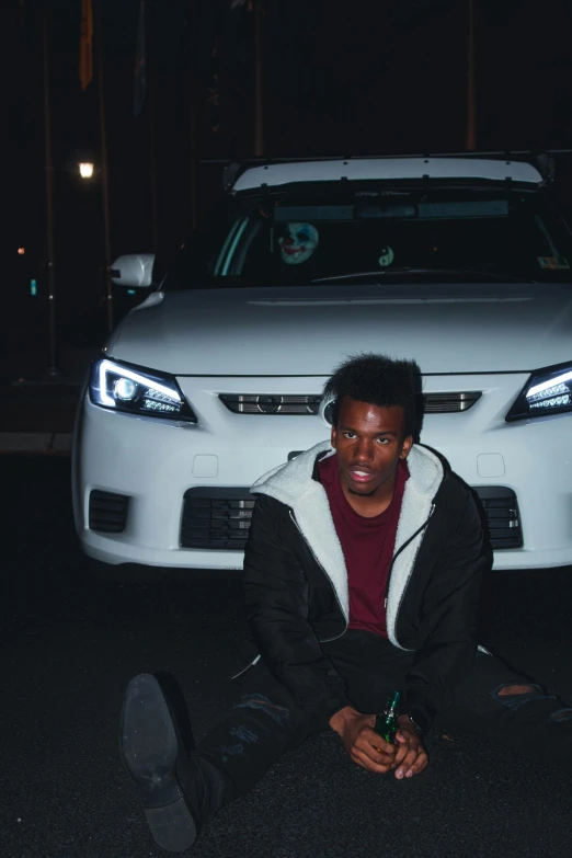 a man sitting on the ground in front of a car, dark skinned, cross-eyed, sythwave, headlights turned on