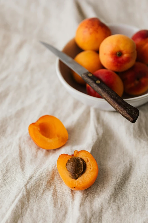 a bowl of apricots and a knife on a table, trending on unsplash, still life photo of a backdrop, high quality photo, soft skin, carefully crafted