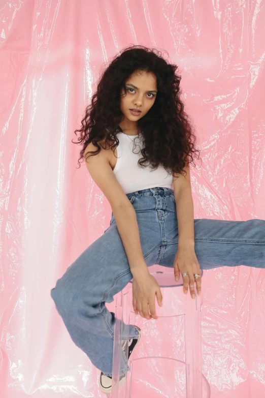 a beautiful young woman sitting on top of a stool, an album cover, featured on instagram, renaissance, baggy jeans, tessa thompson inspired, pastel pink, glossy magazine photoshoot