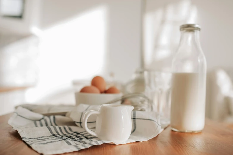 a bottle of milk sitting on top of a wooden table, a still life, pexels contest winner, white tablecloth, with a white mug, background image, an egg