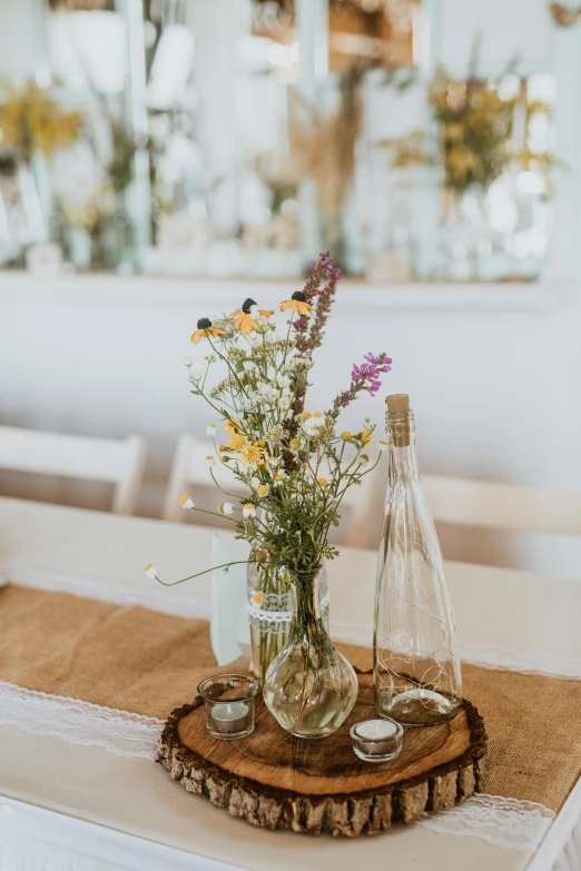 a wooden table topped with vases filled with flowers, unsplash, wild flowers, bottle, centerpiece, white