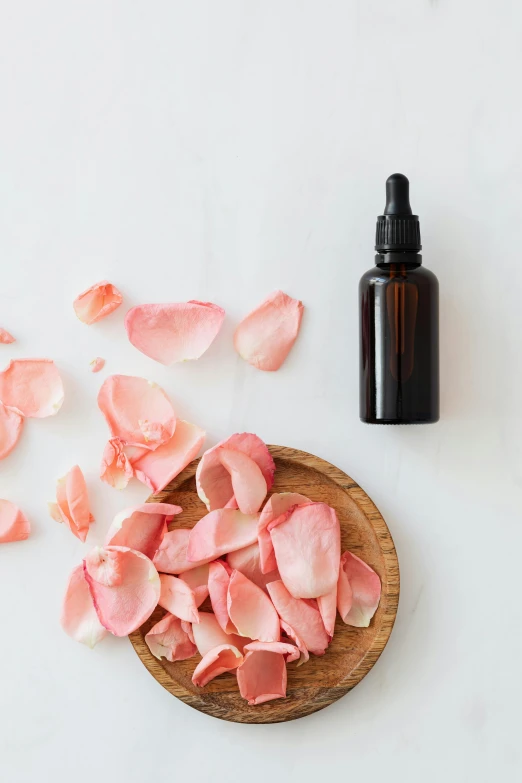 a wooden bowl filled with pink petals next to a bottle of essential oil, by Arabella Rankin, slide show, skin care, thumbnail, rose in hair