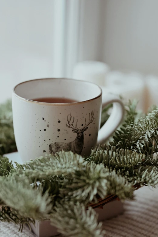 a cup of tea sitting on top of a table, pexels contest winner, folk art, evergreen branches, elk, holiday season, square