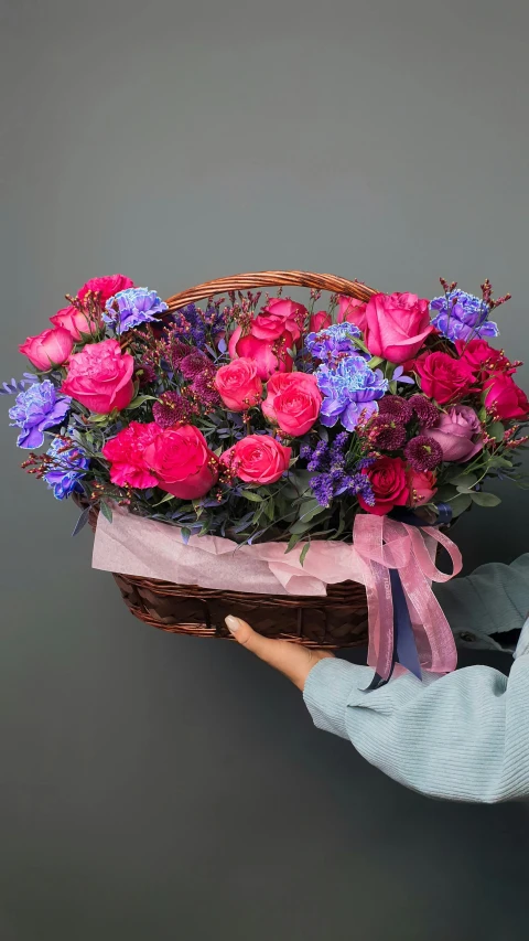 a woman holding a basket of pink and purple flowers, by Valentine Hugo, pexels contest winner, on a gray background, fuchsia and blue, decorative roses, wide scene