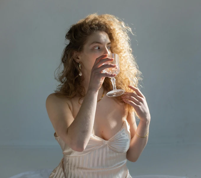 a woman sitting on a bed drinking a glass of wine, inspired by Elsa Bleda, pexels contest winner, renaissance, translucent dress, curly haired, pale as marble, unedited