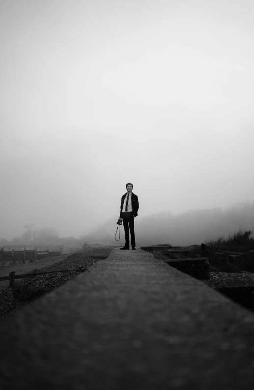 a black and white photo of a man standing on a bridge, by Thomas Fogarty, conceptual art, fog on the ground, new album cover, gentleman, ((portrait))