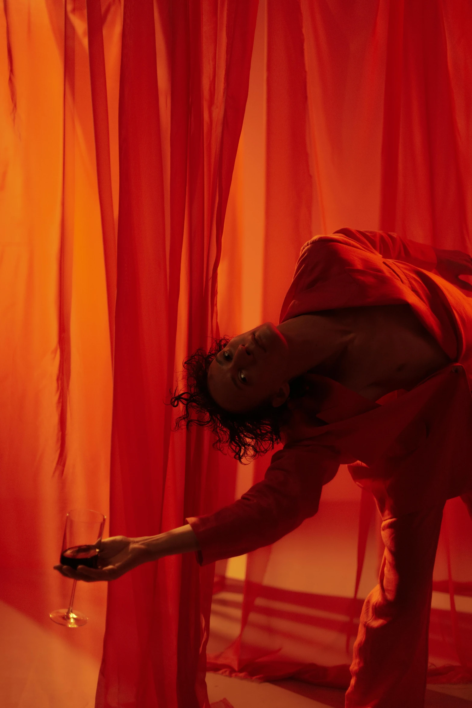 a woman standing in front of a red curtain, inspired by Carrie Mae Weems, pexels contest winner, dramatic floating pose, red and orange glow, performance, dolman