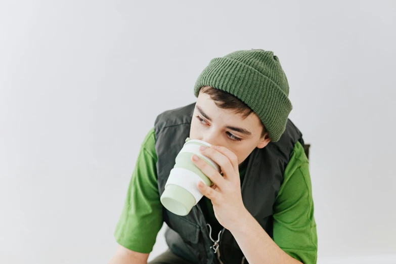 a young man sitting on a bed drinking from a cup, by Nicolette Macnamara, trending on pexels, green visor, aussie baristas, billie eilish, moringa juice