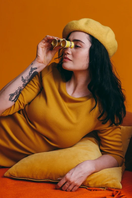 a woman sitting on a couch looking through a pair of binoculars, inspired by Elsa Bleda, trending on pexels, renaissance, yellow overall, holding hot sauce, alluring plus sized model, yellow cap