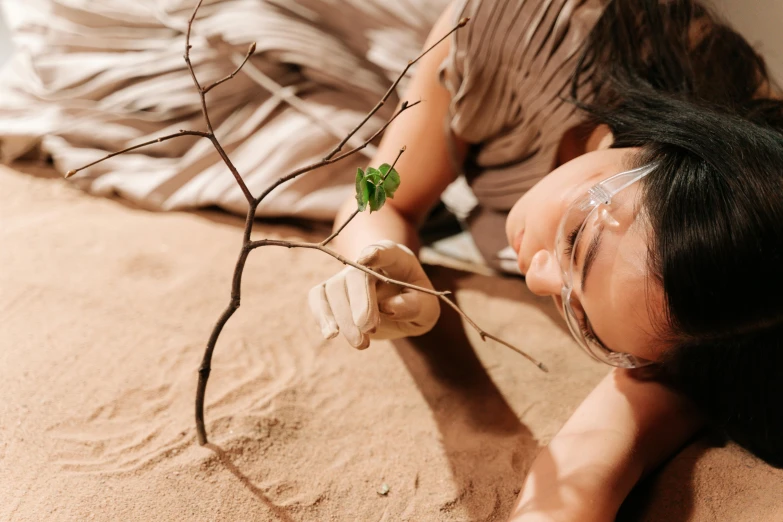 a woman laying on the ground with a plant in her hand, trending on pexels, environmental art, the australian desert, plants in glasses, avatar image, root system