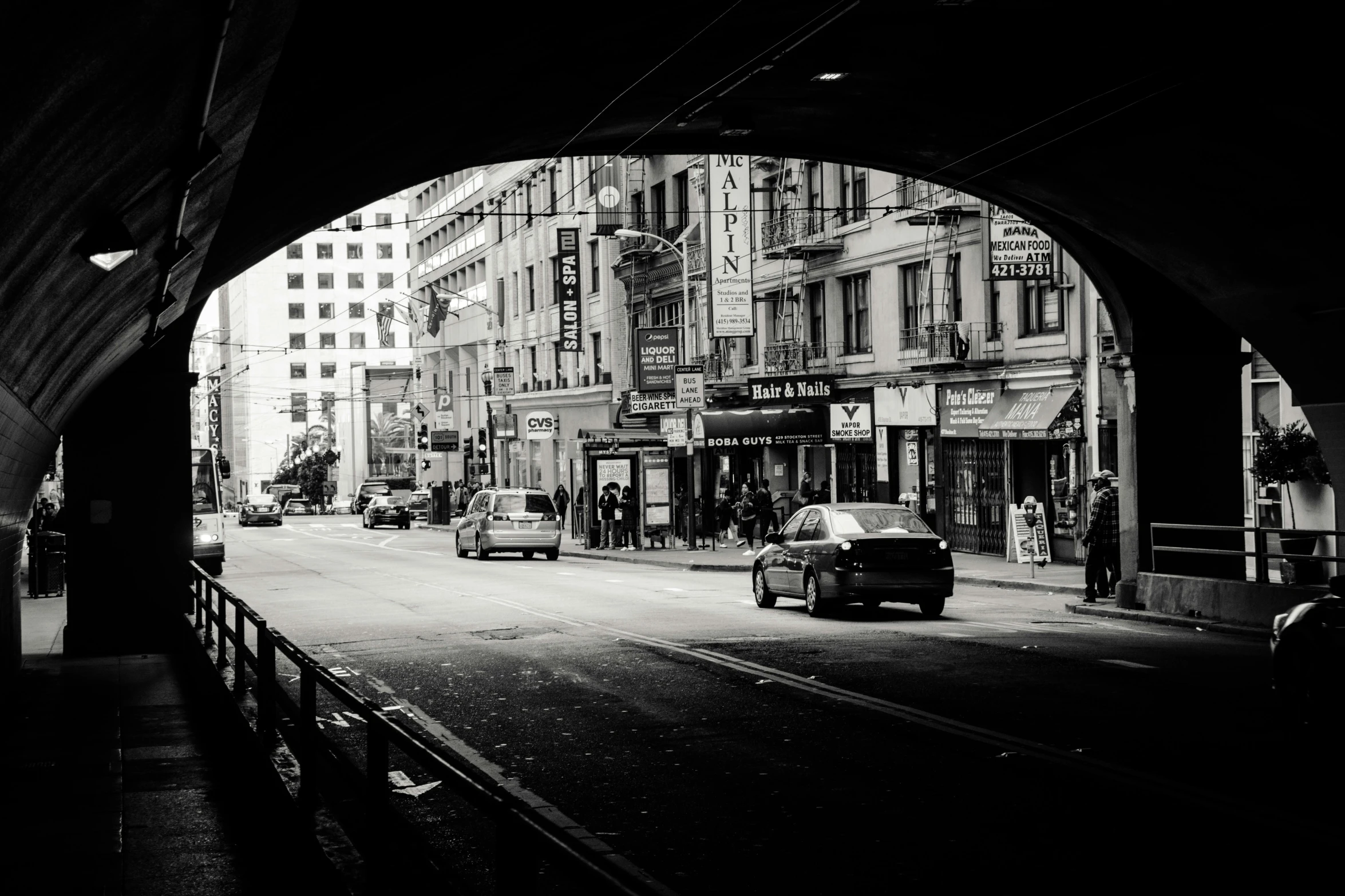 a black and white photo of a city street, inspired by Vivian Maier, unsplash contest winner, under bridge, cyberpunk elevated train, 2000s photo, view from across the street