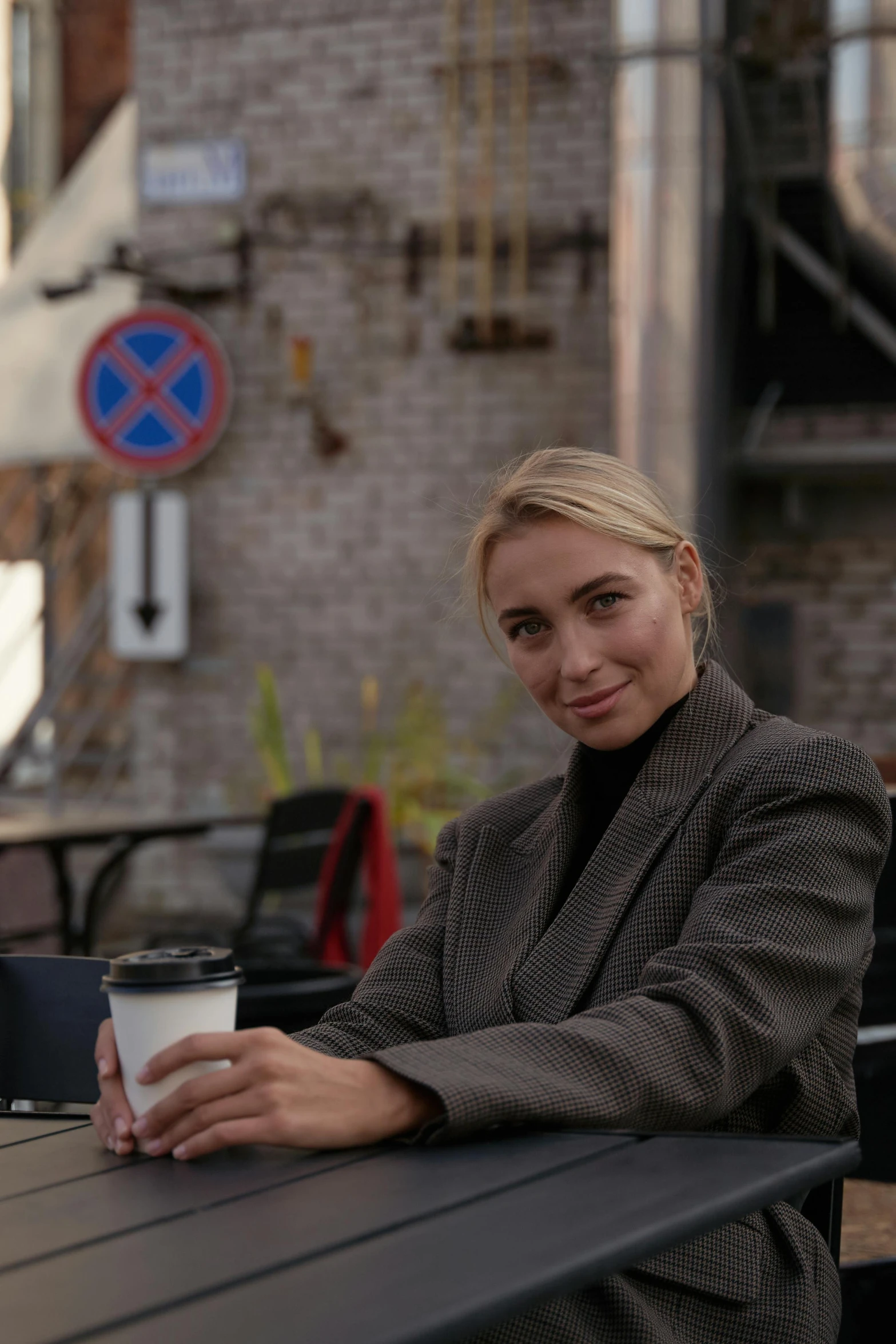 a woman sitting at a table with a cup of coffee, trench coat and suit, olya bossak, in town, blonde swedish woman