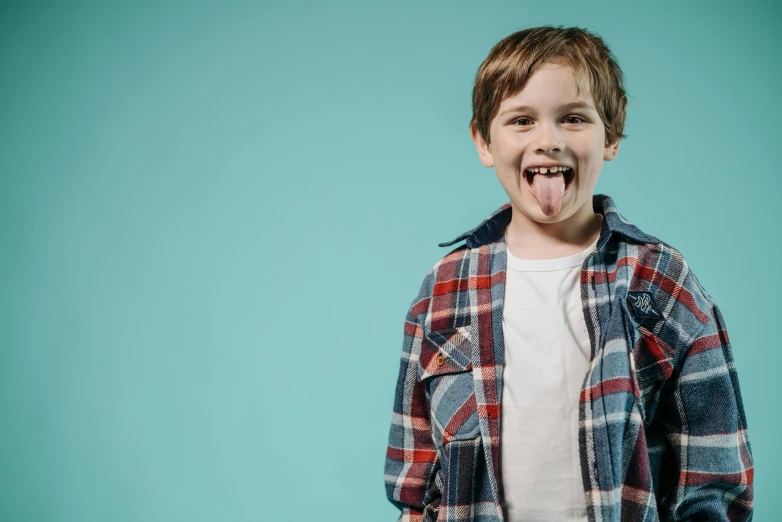 a young boy making a funny face with his tongue, an album cover, by Lee Gatch, pixabay, wearing a plaid shirt, teal studio backdrop, 15081959 21121991 01012000 4k, future activist