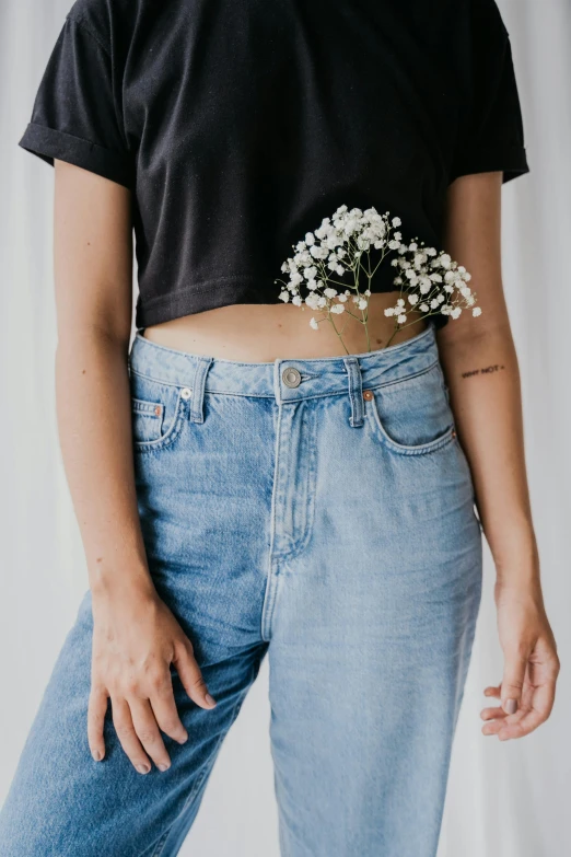 a woman wearing a black crop top and jeans, a colorized photo, inspired by Sydney Carline, trending on unsplash, gypsophila, tattoo style, bouquet, minimal clothing