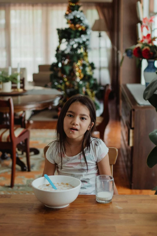 a little girl sitting at a table with a bowl of cereal, a portrait, pexels contest winner, holiday season, at a dinner table, gif, low ultrawide shot