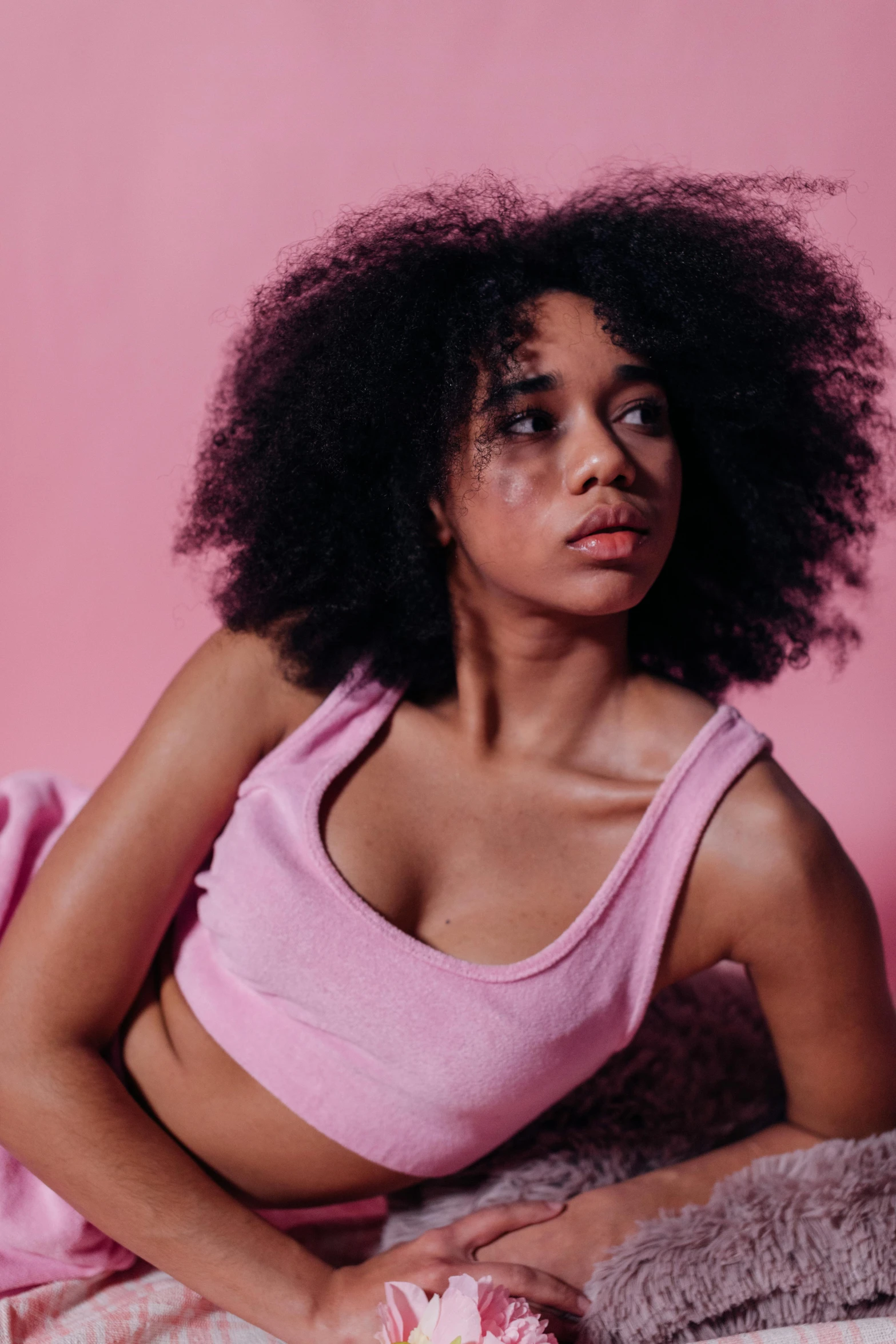 a beautiful young woman laying on top of a bed, by Dulah Marie Evans, trending on pexels, process art, pink halter top, black curly hair, looking confused, sitting on a couch