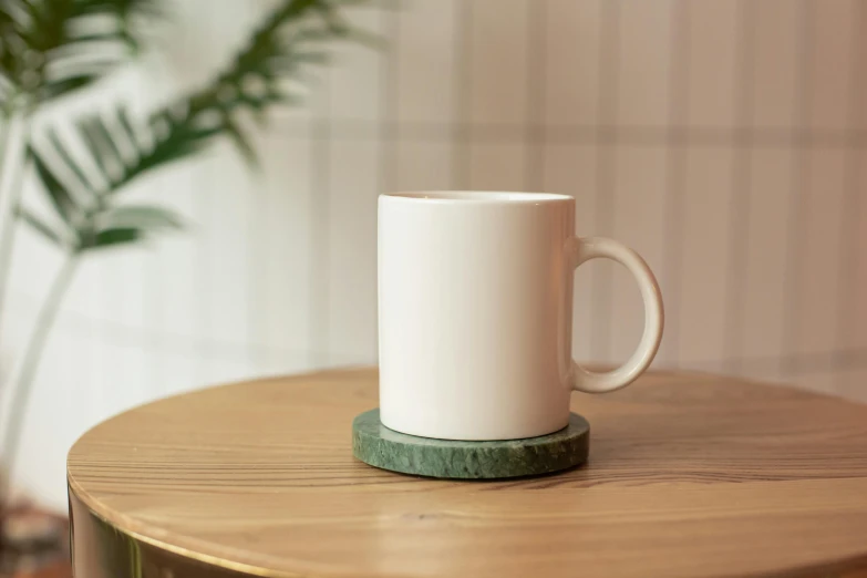 a white coffee cup sitting on top of a wooden table, inspired by Art Green, private press, thin porcelain, felt, round base, green: 0.5