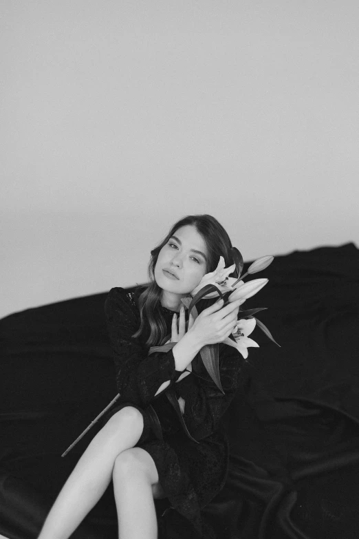 a black and white photo of a woman sitting on a bed, a black and white photo, by Silvia Pelissero, unsplash, art nouveau, lucy hale, draped in velvet and flowers, anna kendrick, album