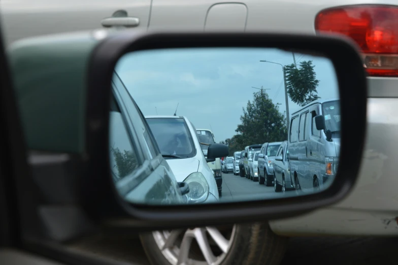 a rear view mirror on the side of a car, heavy traffic, cars parked underneath, in the distance, a head-on