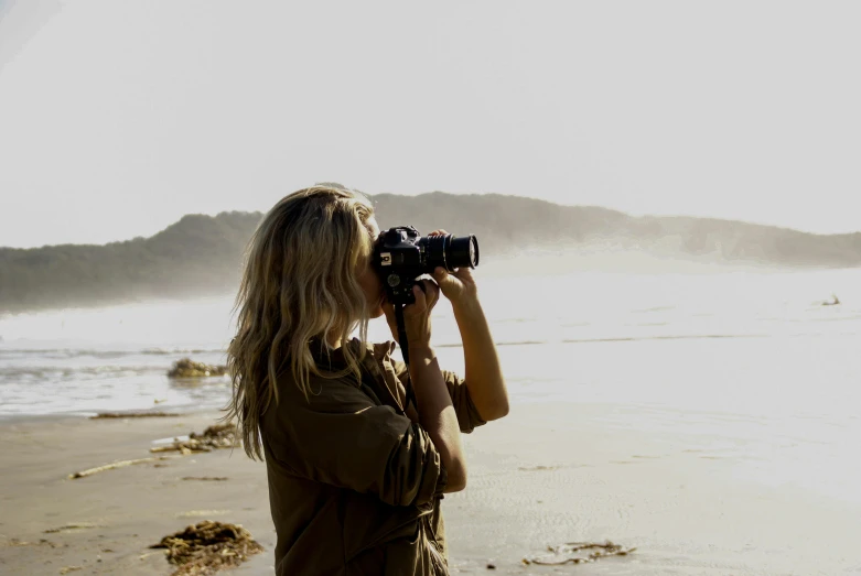 a woman standing on top of a beach holding a camera, profile image, soft-sanded coastlines, telephoto long distance shot, instagram picture