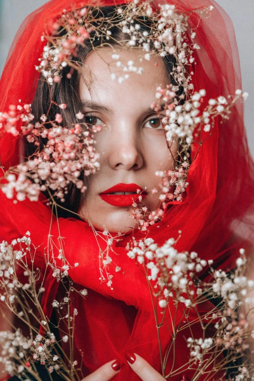 a woman wearing a red veil and holding flowers, inspired by Elsa Bleda, femalev beauty, red cheeks, holiday season, with soft bushes