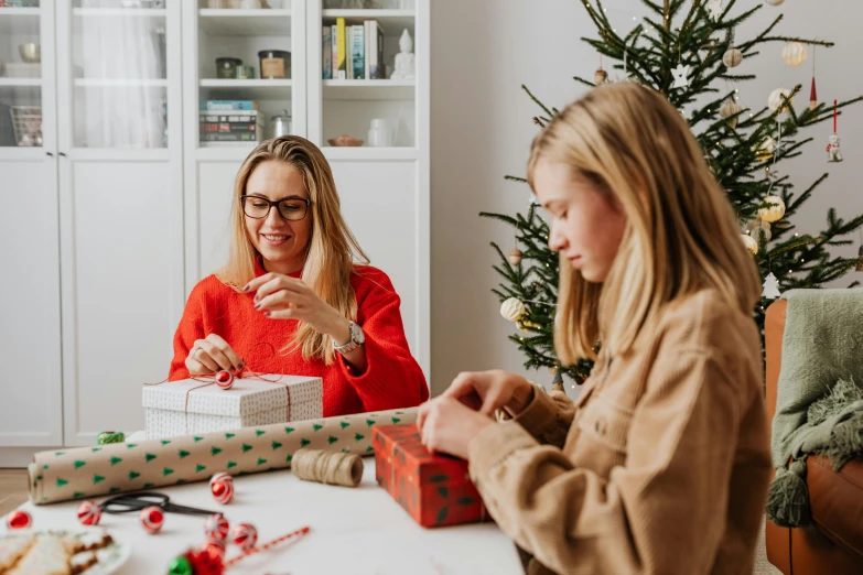 two women sitting at a table in front of a christmas tree, by Emma Andijewska, pexels contest winner, birthday wrapped presents, avatar image, paper quilling, teenager girl