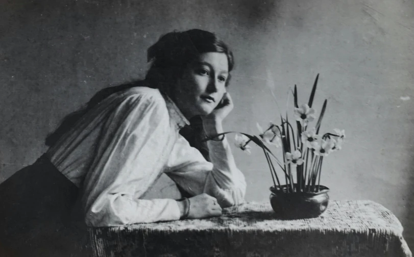 a black and white photo of a woman leaning on a table, by Antonin Artaud, art nouveau, sitting with flowers, frederick judd waugh, may gibbs, catalog photo