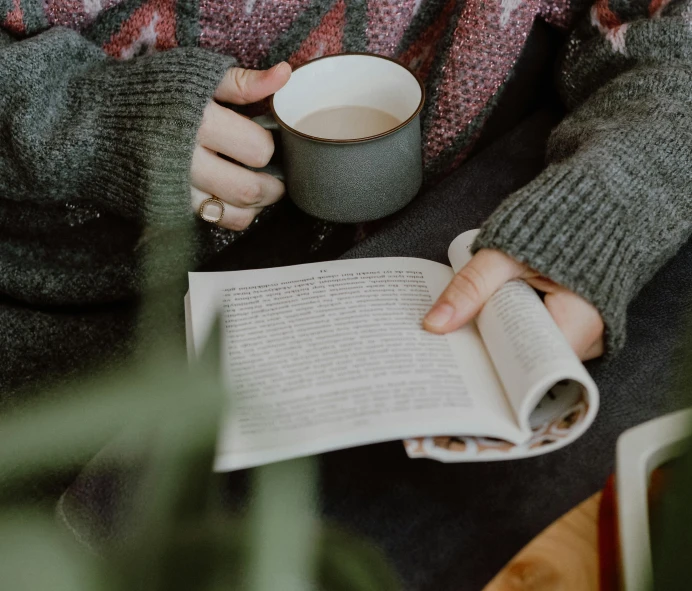 a woman reading a book while holding a cup of coffee, by Emma Andijewska, pexels contest winner, grey, thumbnail, background image, cottagecore hippie
