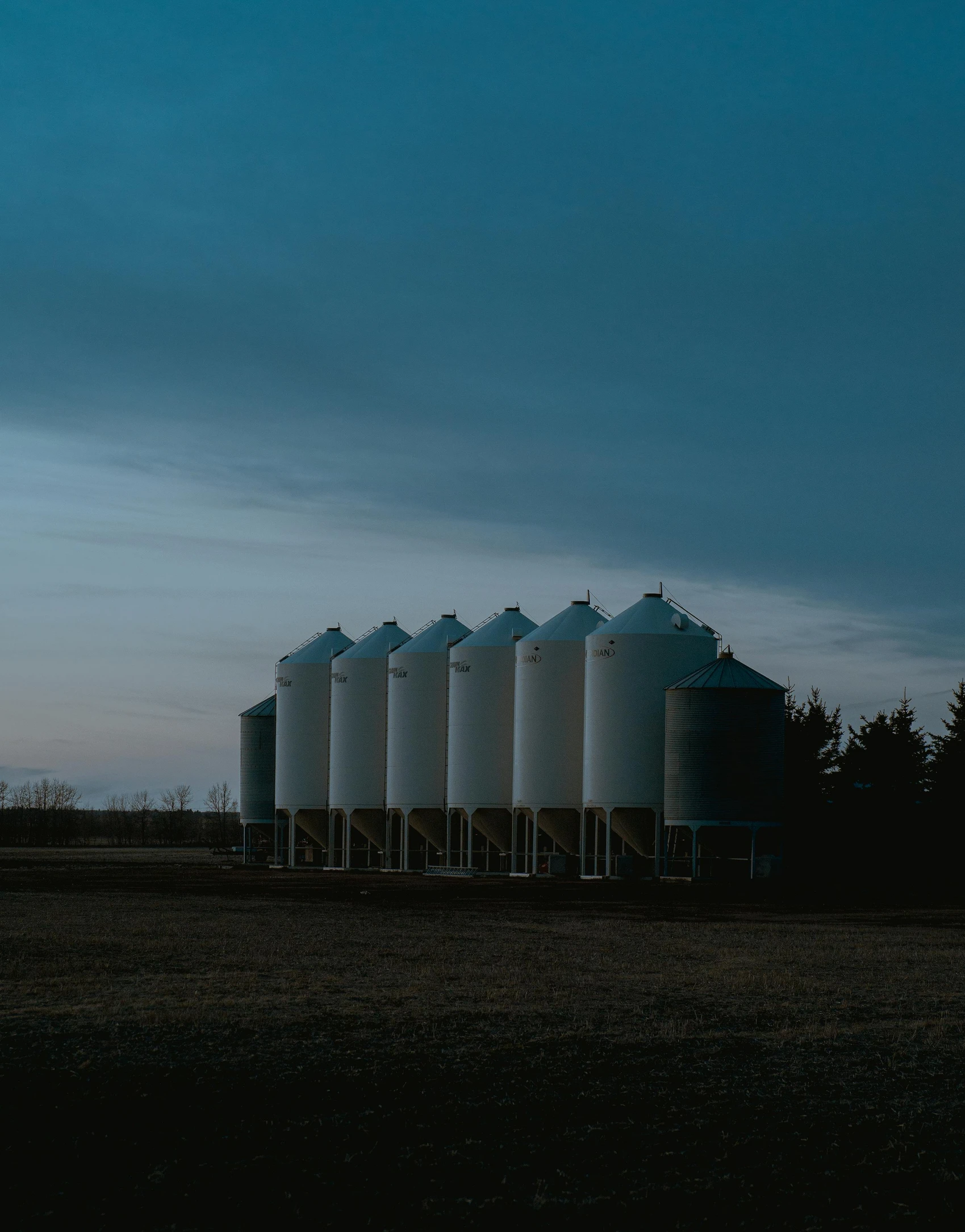 a row of silos sitting in the middle of a field, pexels contest winner, dusk light, trending on vsco, feed troughs, low quality photo