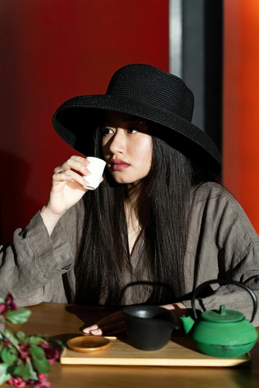 a woman sitting at a table with a cup of tea, an album cover, inspired by Itō Shinsui, unsplash, black hat, black long hair, candid portrait photo, ethnicity : japanese