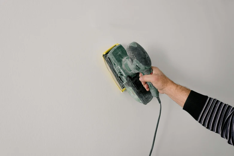 a person using a sander on a wall, inspired by Lucio Fontana, instagram, hyperrealism, light grey backdrop, green light dust, official product photo, facing front
