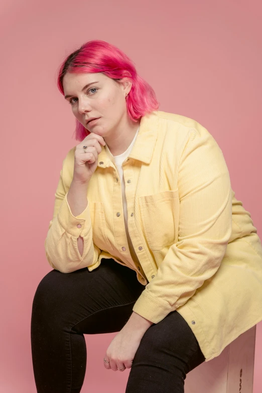 a woman with pink hair sitting on a stool, yellow backdrop, wearing a jeans jackets, josh grover, obese )