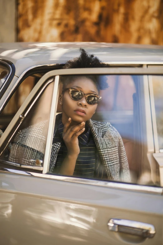 a woman sitting in the passenger seat of a car, inspired by Gordon Parks, trending on pexels, afrofuturism, thin round glasses, vintage aston martin, casually dressed, pastel'