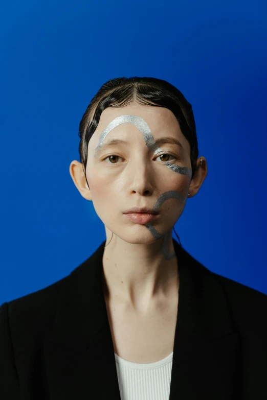 a woman with white paint on her face, an album cover, inspired by Gao Cen, neo-dada, with blue skin, yasumoto oka, genderless, looking away from camera