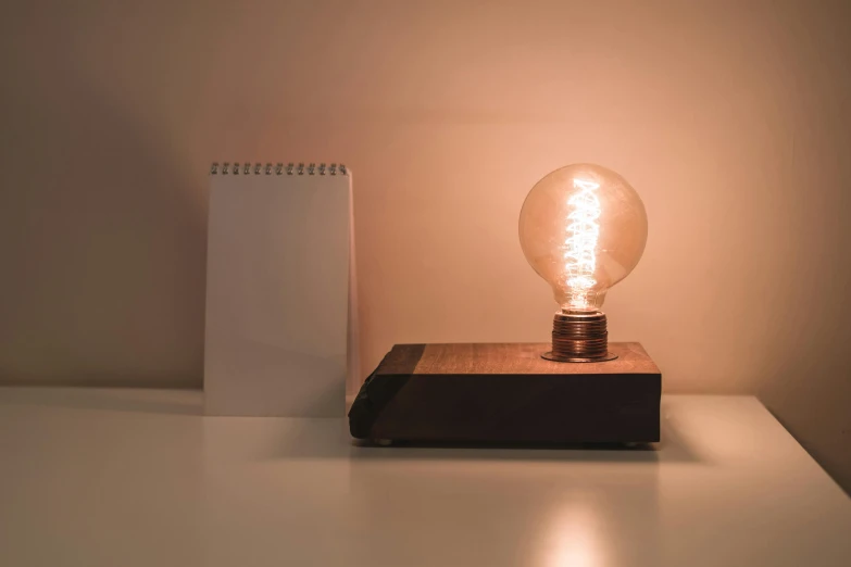 a light bulb sitting on top of a wooden block, inspired by George Fiddes Watt, kinetic art, minimalist desk, brown, instagram post, nightlight study