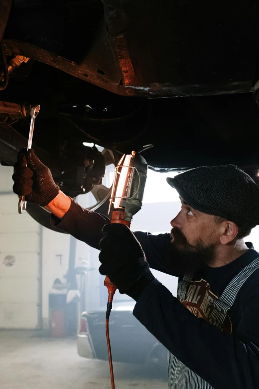 a man working on a vehicle in a garage, a portrait, featured on reddit, renaissance, roth's drag nut fuel, low angle shot, bearded and built, leaking