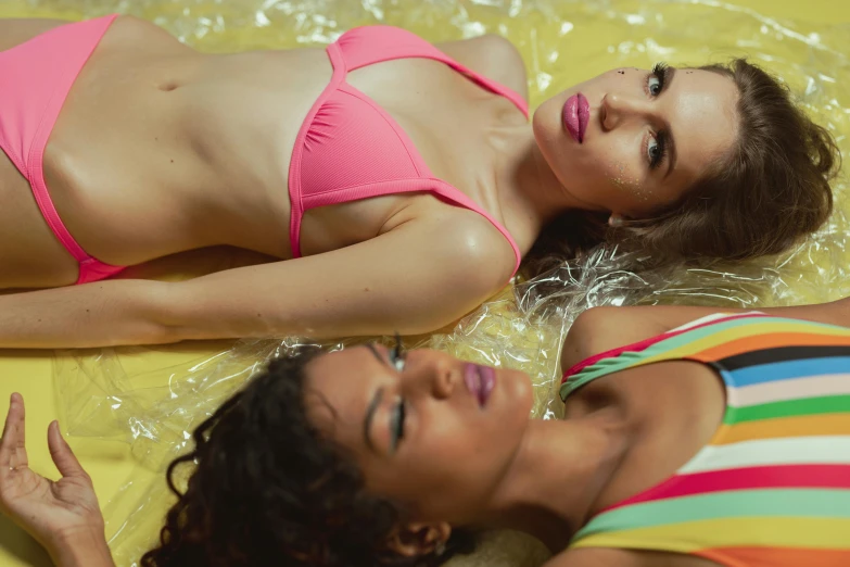 a couple of women laying on top of a bed, inspired by Elsa Bleda, trending on pexels, figuration libre, pink and yellow, attire: bikini, seapunk, plastic skin