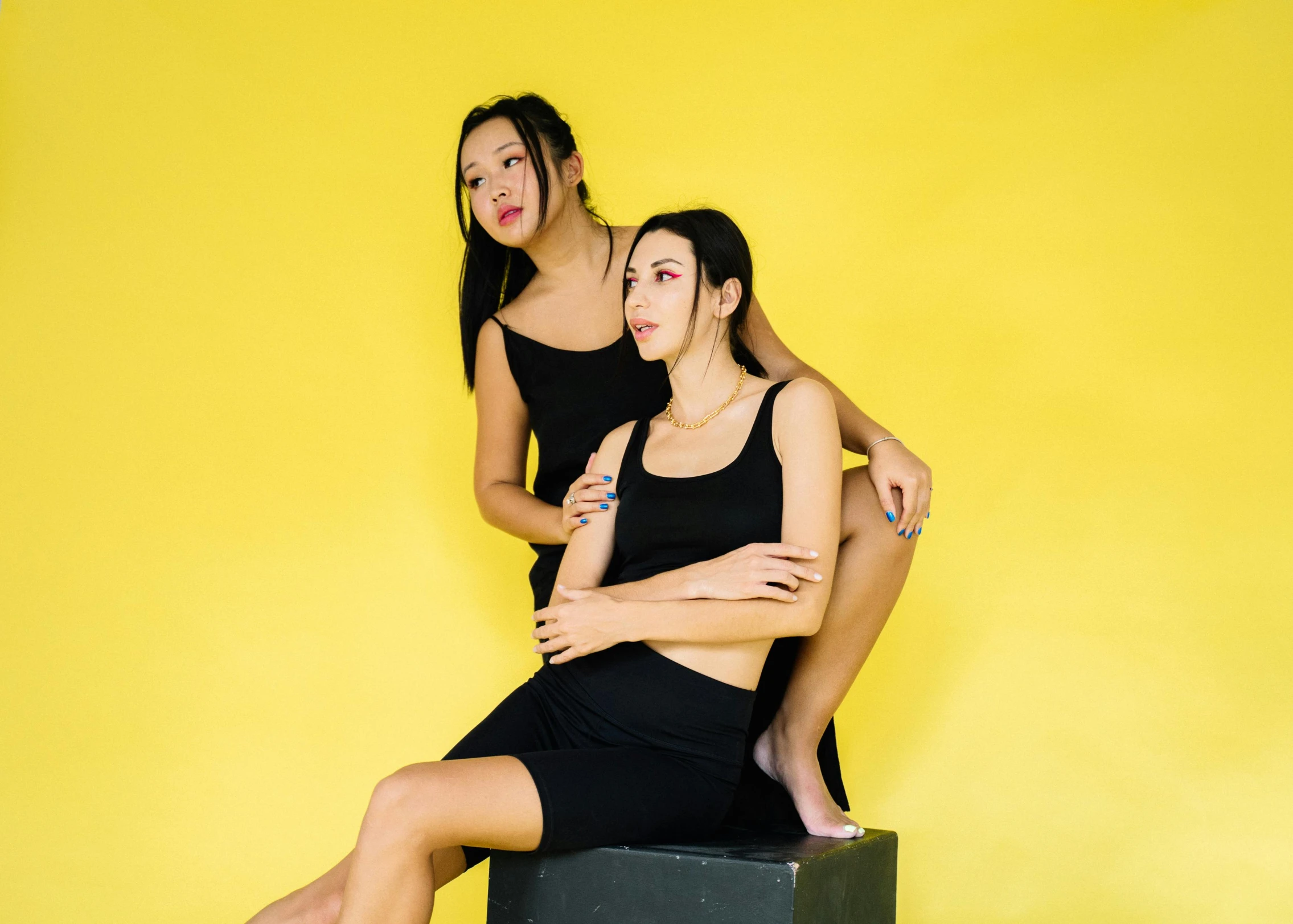 a couple of women sitting on top of a box, inspired by Wang Duo, trending on pexels, black. yellow, delicate poses, asian features, black outfit