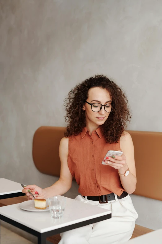 a woman sitting at a table using a cell phone, a portrait, trending on pexels, renaissance, brown curly hair, wearing business casual dress, terracotta, girl with glasses