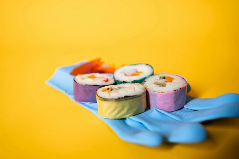 a person in a blue glove holding a plate of sushi, a colorized photo, by Julia Pishtar, unsplash, pop art, molecular gastronomy, cloth wraps, cute colorful adorable, yellow