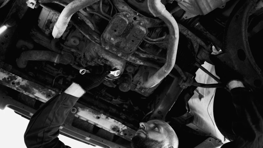 a black and white photo of a man working on a vehicle, a portrait, by Kristian Zahrtmann, auto-destructive art, underside, bald orc mechanic, 🌸 🌼 💮, high quality upload