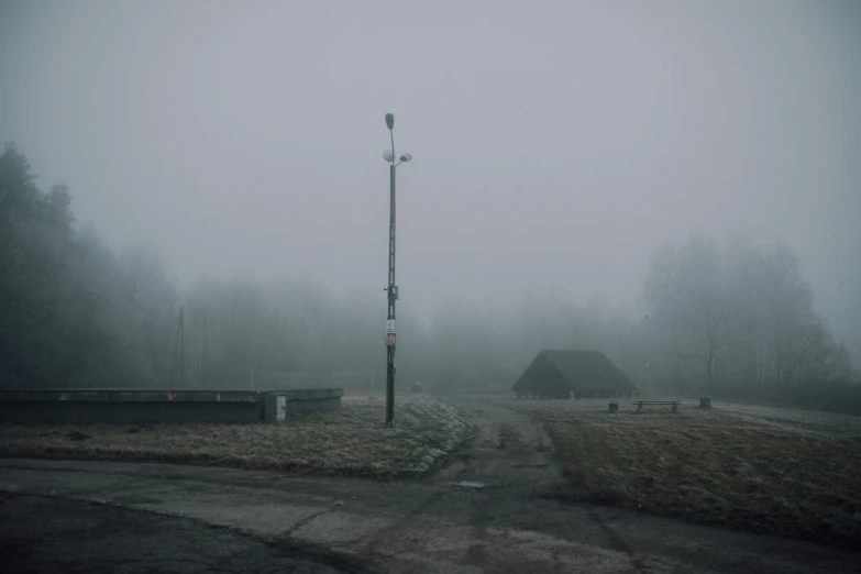 a street light sitting on the side of a road, by Attila Meszlenyi, under a gray foggy sky, military base, a park, sandra pelser