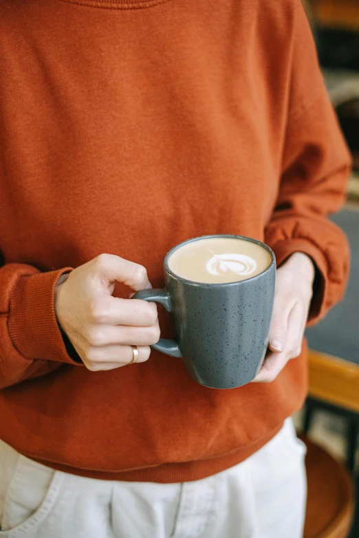 a close up of a person holding a cup of coffee, by Jessie Algie, happening, long orange sweatshirt, slate, thumbnail, cafe