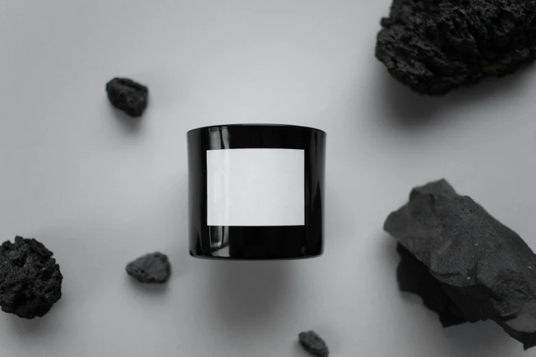 a candle sitting on top of a table surrounded by rocks, a black and white photo, unsplash, bauhaus, made of smooth black goo, shungite bangle, advertising photo, vantablack gi