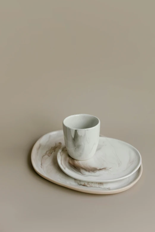a cup and saucer sitting on a plate, a marble sculpture, inspired by Josefina Tanganelli Plana, dau-al-set, beige mist, made of clay, 10k, white sky