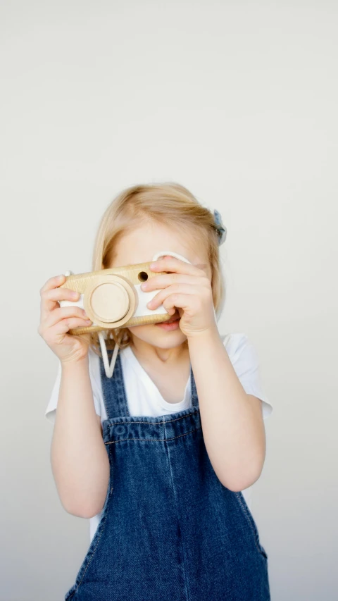 a little girl holding a camera up to her face, wooden, yellow, small, set against a white background