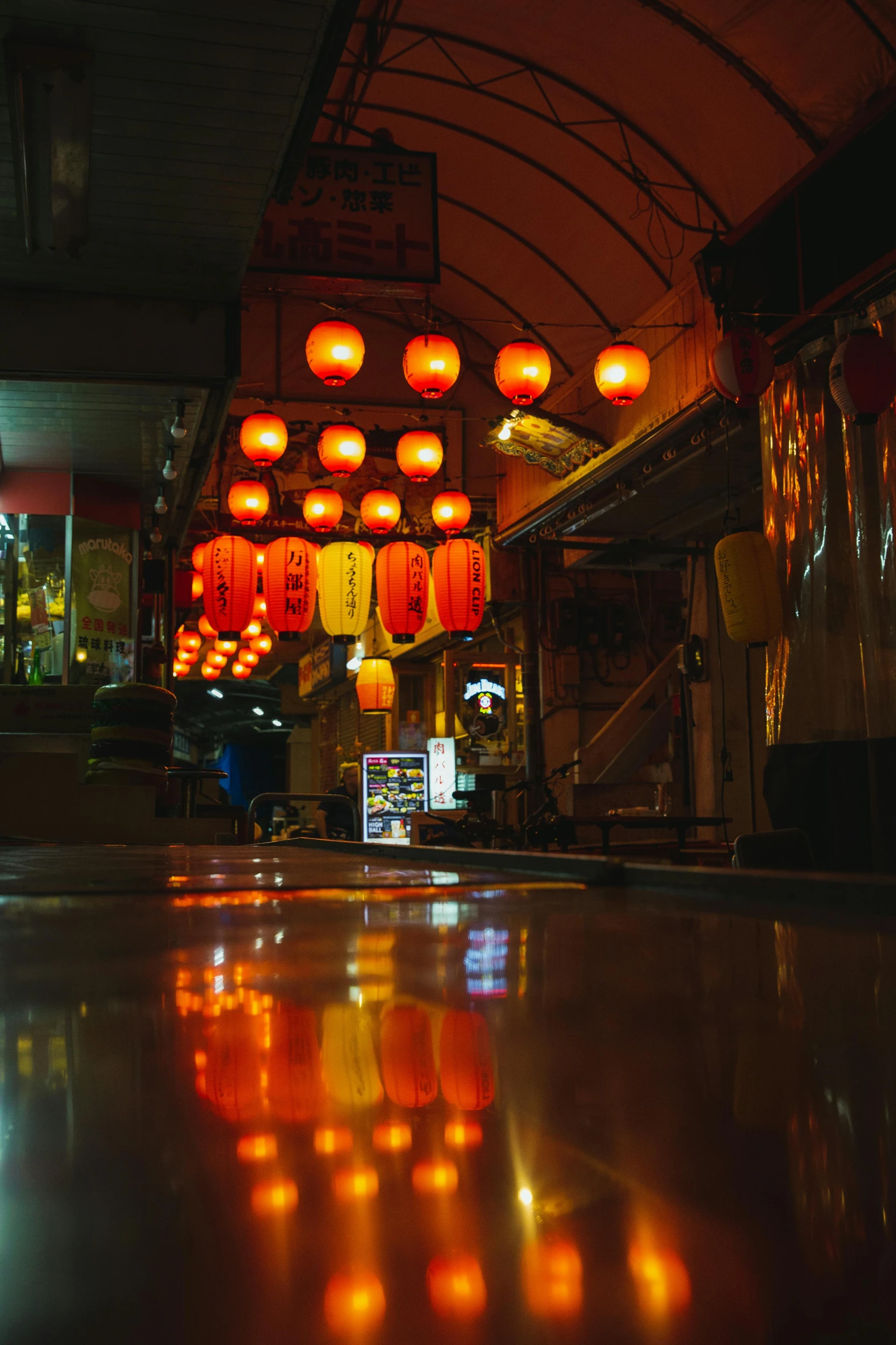 a group of red lanterns hanging from the ceiling, mingei, with orange street lights, reflections on wet streets, inside a bar, deserted