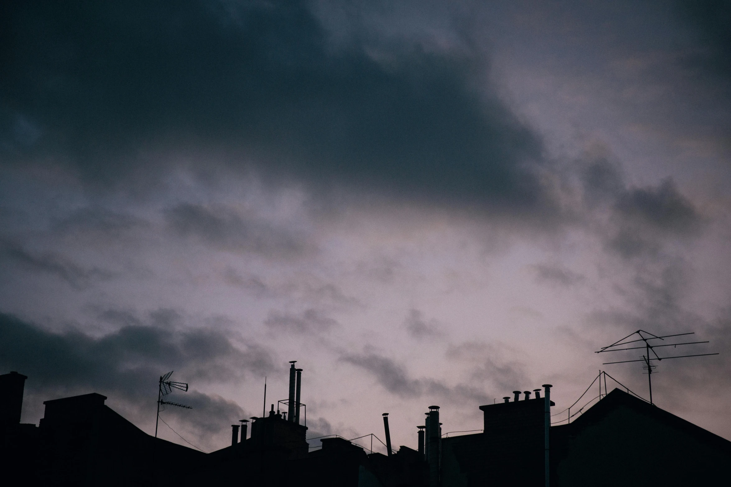 a sky filled with lots of dark clouds, inspired by Elsa Bleda, pexels contest winner, aestheticism, chimneys on buildings, early evening, dark purple sky, hiding in the rooftops